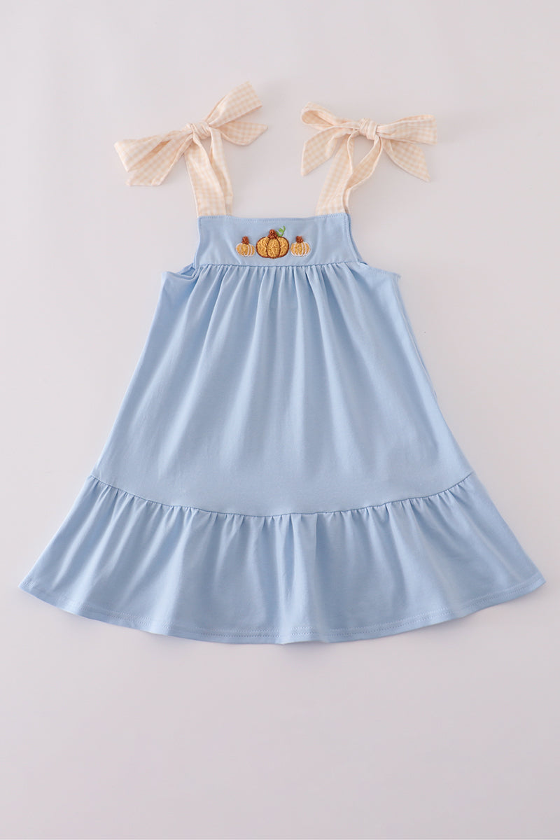 Light blue dress with pumpkin embroidery and bow straps on a light gray background