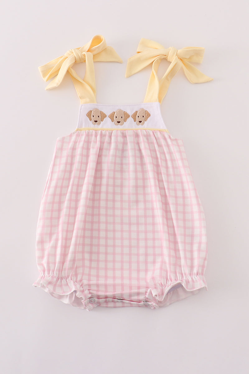 Pink gingham baby romper with yellow straps and bow accents on a light gray background