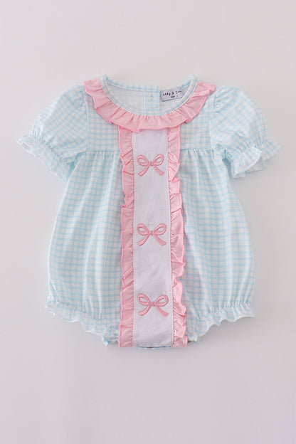 Baby romper with checkered pattern and pink ribbons on a light gray background