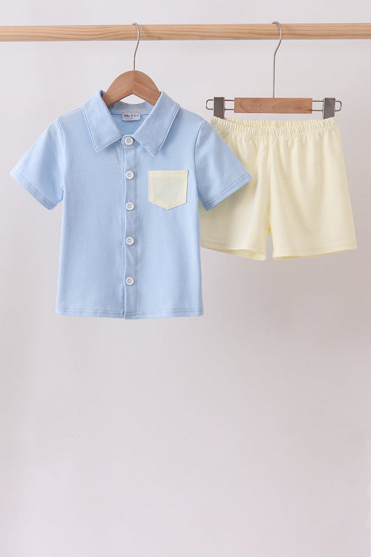 Light blue shirt and yellow shorts hanging on a wooden rack against a white background