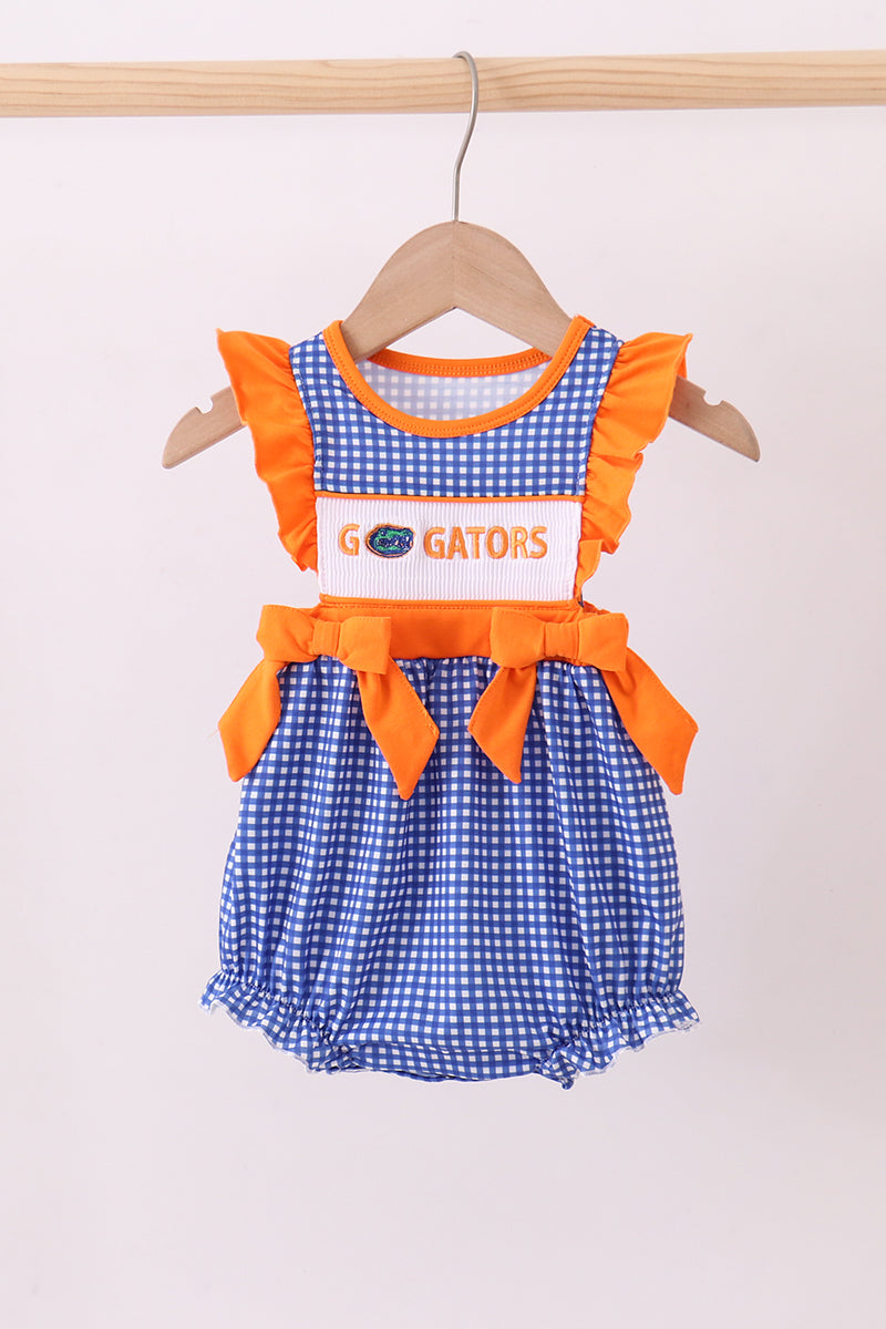 Children's outfit with blue checkered dress and orange accents on a hanger against a white background
