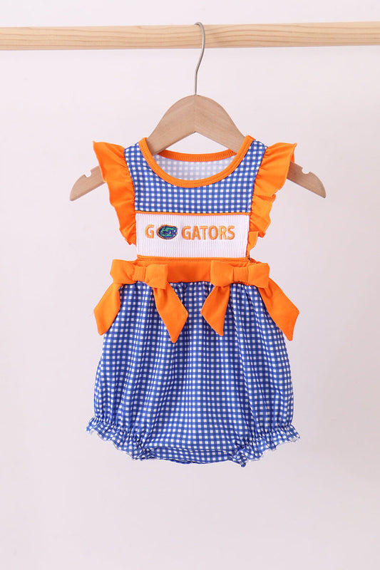 Children's outfit with blue checkered dress and orange accents on a hanger against a white background