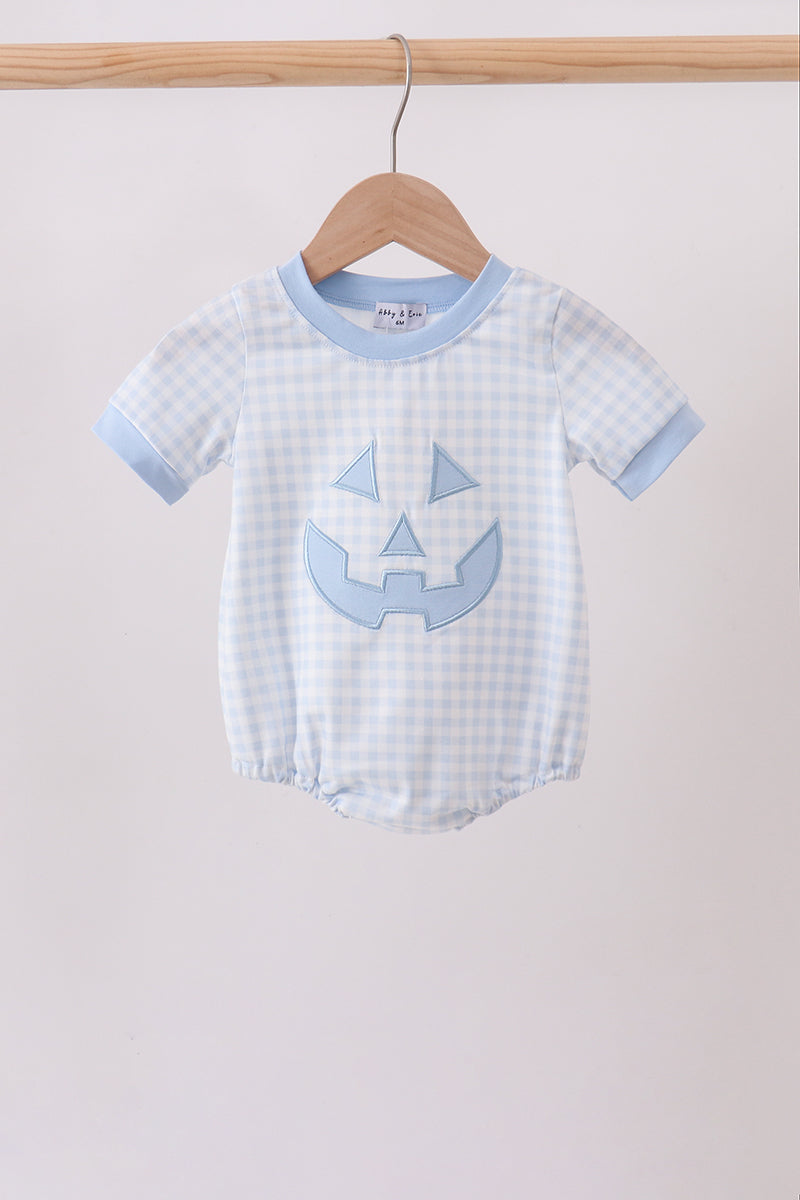 A baby short-sleeve romper in a light blue and white gingham pattern, featuring a light blue pumpkin face applique on the front and light blue ribbed trim, hanging on a wooden hanger.