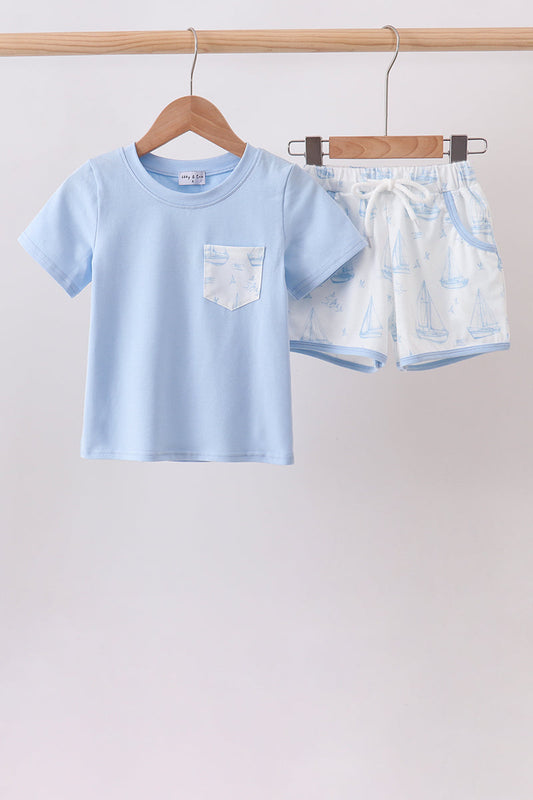 A children's two-piece clothing set hanging on wooden hangers from a wooden rod. The set includes a light blue short-sleeve crewneck t-shirt with a chest pocket and matching light blue and white nautical print shorts with a white drawstring.