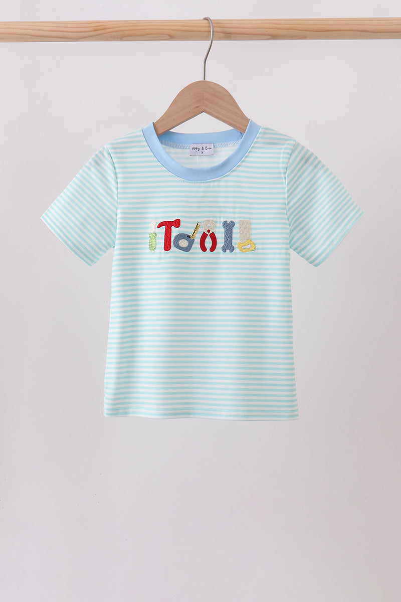 A light blue and white striped short-sleeve baby t-shirt hanging on a wooden hanger. The shirt features a light blue crew neck and a colorful graphic on the chest spelling 'TOY' using different colored letters.
