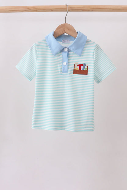 A children's short-sleeve polo shirt hanging on a wooden hanger against a plain light background. The shirt has thin mint green and white horizontal stripes, a light blue collar, a light blue placket with a white button, and a small embroidered patch on the chest showing a pencil box with colorful pencils and a red letter.