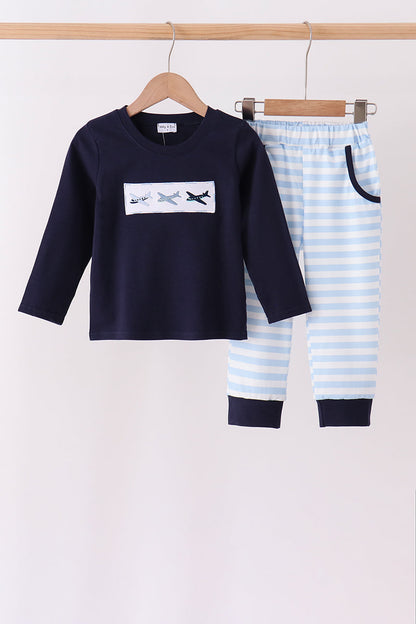 A two-piece children's outfit hanging on wooden hangers against a plain light background. The set includes a navy long-sleeve top with a white chest graphic showing three small airplanes, and matching navy-and-white striped pants with dark navy pocket trim and cuffs.