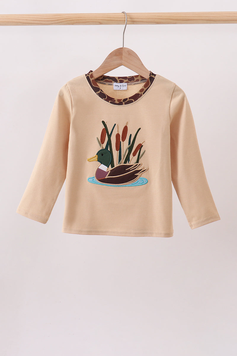 A beige long-sleeve baby/toddler top hanging on a wooden hanger, featuring a duck and reeds graphic on the front and a leopard-print collar.