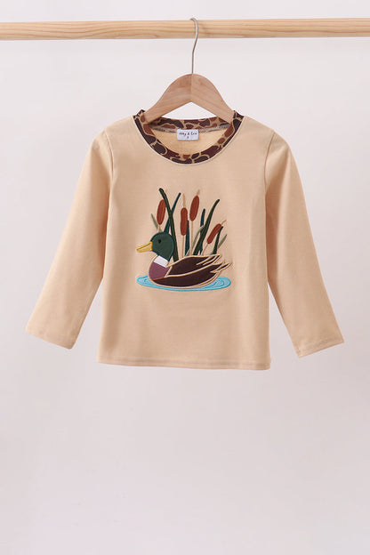 A beige long-sleeve baby/toddler top hanging on a wooden hanger, featuring a duck and reeds graphic on the front and a leopard-print collar.