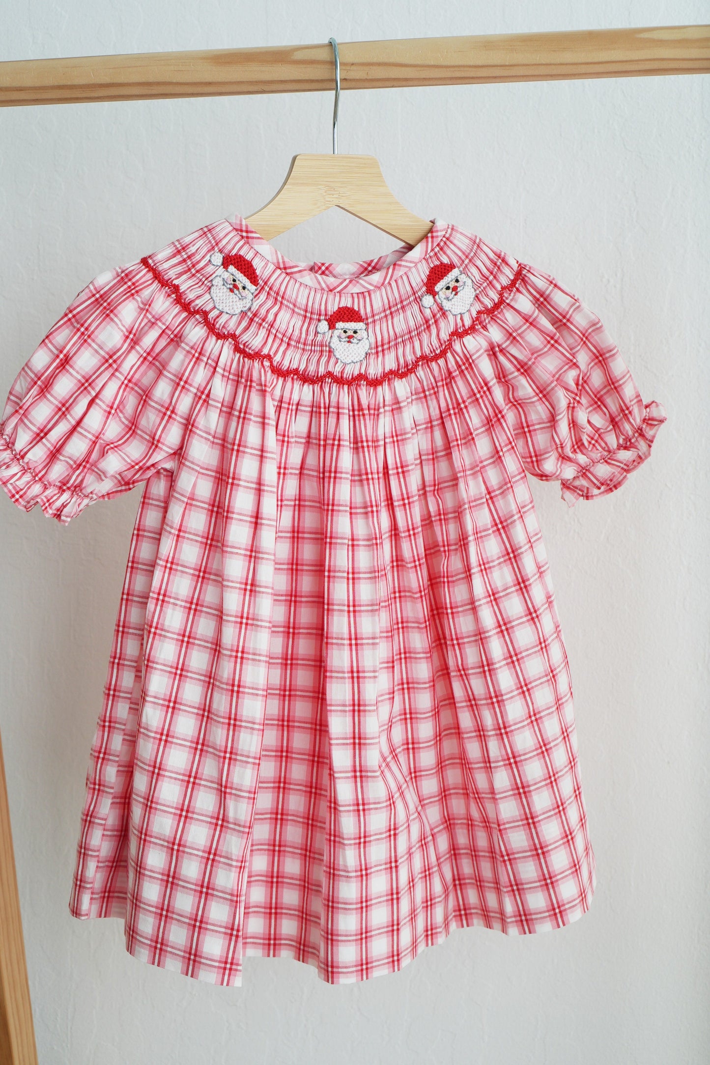 Red and white checkered dress with puff sleeves on a wooden hanger against a white background