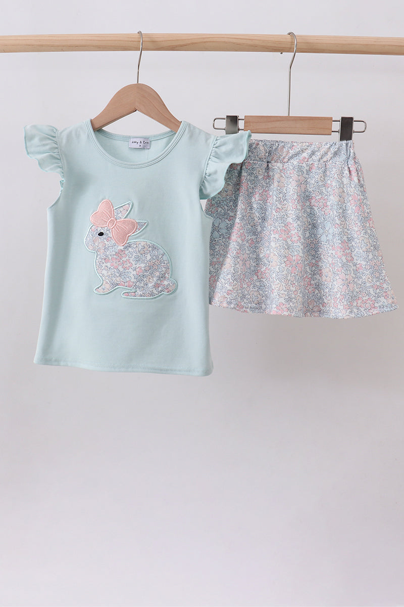 Children's outfit with light blue top and floral skirt on hangers against a plain background