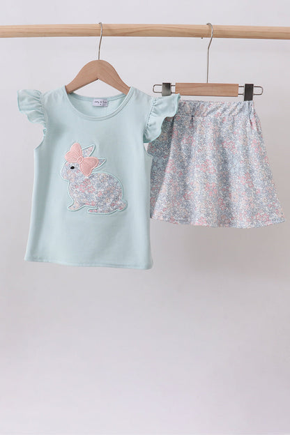 Children's outfit with light blue top and floral skirt on hangers against a plain background