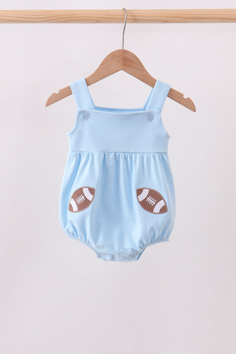 A light blue baby romper with football patch details on the front pockets, hanging on a wooden hanger against a plain light background.