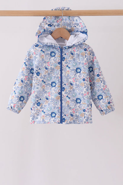 A children's hooded jacket with a light blue, white, and pink floral pattern, hanging on a wooden hanger from a wooden clothes rack against a plain light gray background.