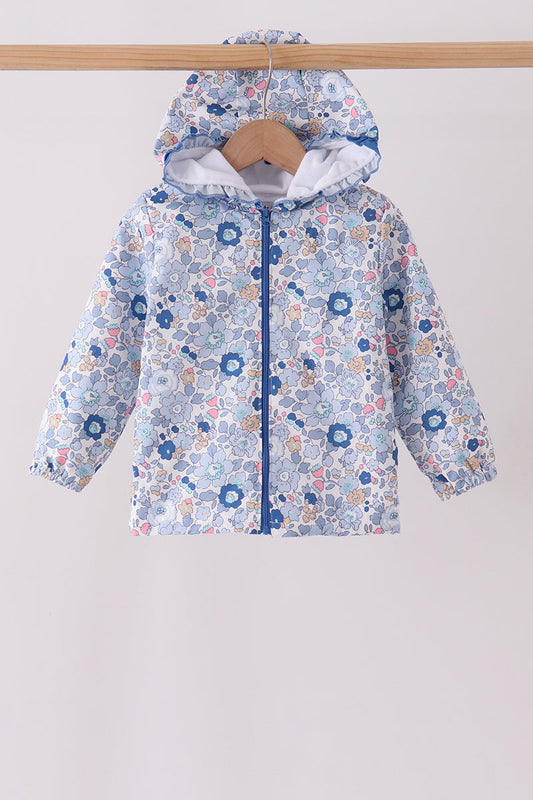 A children's hooded jacket with a light blue, white, and pink floral pattern, hanging on a wooden hanger from a wooden clothes rack against a plain light gray background.