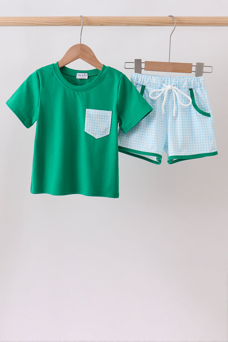 Green t-shirt with a pocket and matching shorts on hangers against a white background