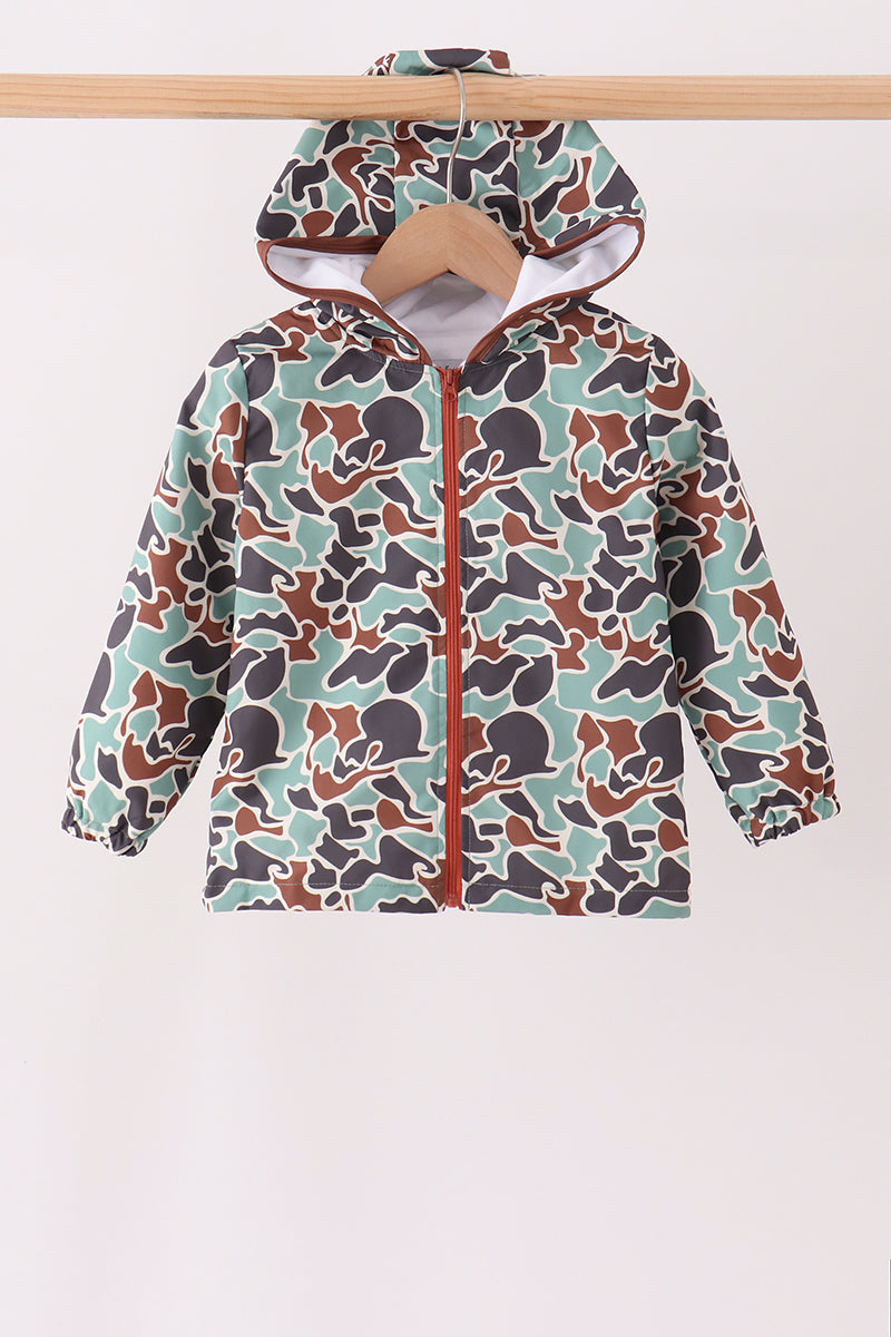 A hooded zip-up jacket with a camouflage pattern in sage green, brown, and dark gray, hanging on a wooden hanger against a plain light background.