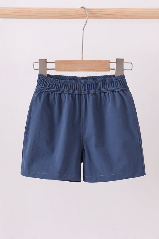 Blue shorts hanging on a wooden hanger against a light background