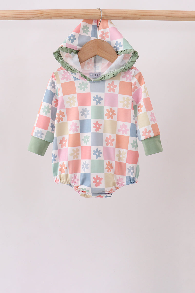 A baby hooded romper with a pastel checkered pattern and floral motifs, hanging on a wooden hanger from a wooden clothes rack against a plain light background.