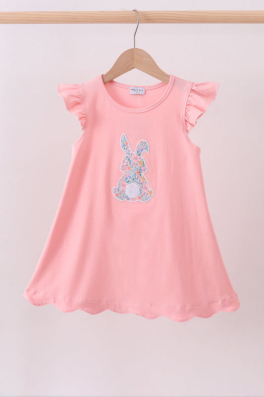 Pink dress with floral bunny design on a wooden hanger against a light background