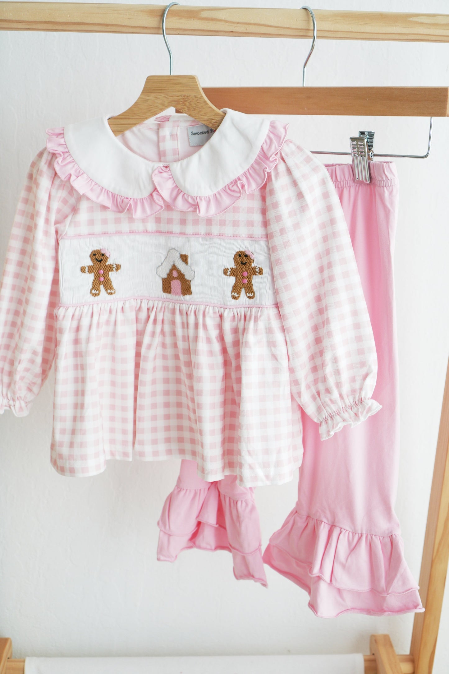 Pink checkered outfit with gingerbread design on a hanger against a white background