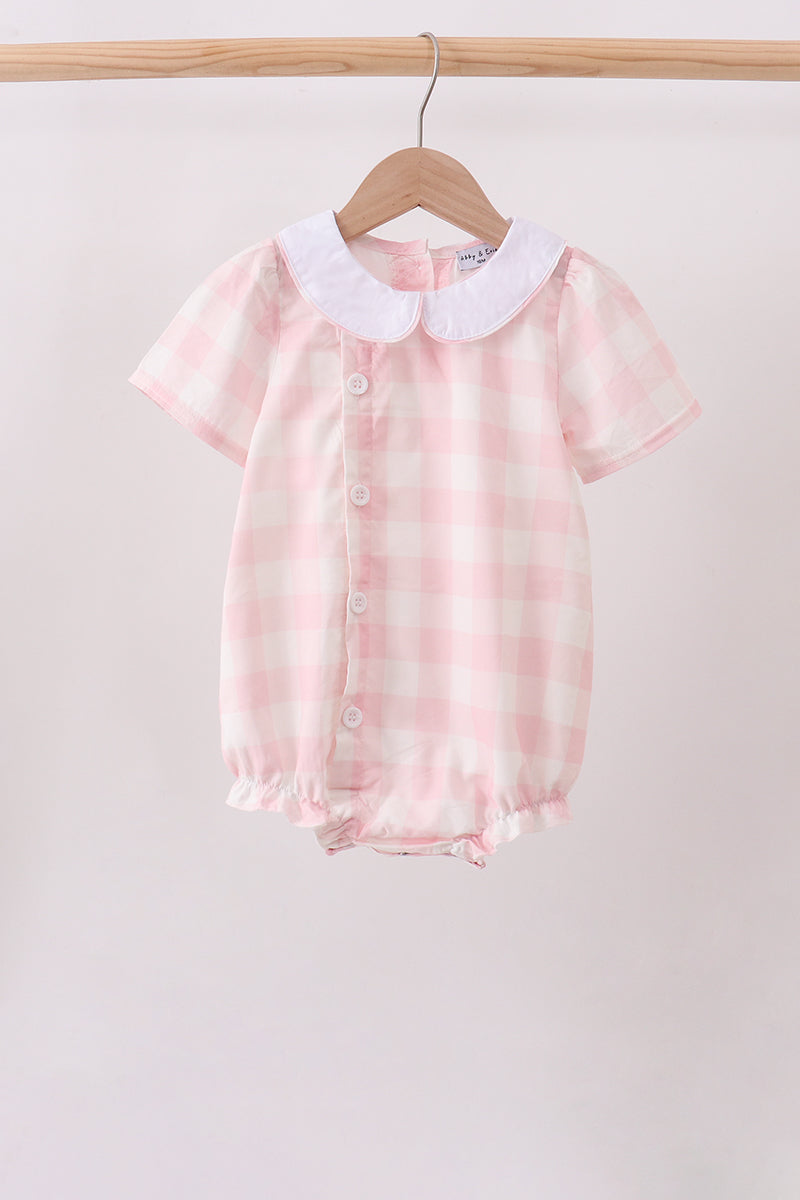 A baby short-sleeve romper in a pink and white gingham check pattern, featuring a white Peter Pan collar and front snap buttons, hanging on a wooden hanger from a clothing rack.