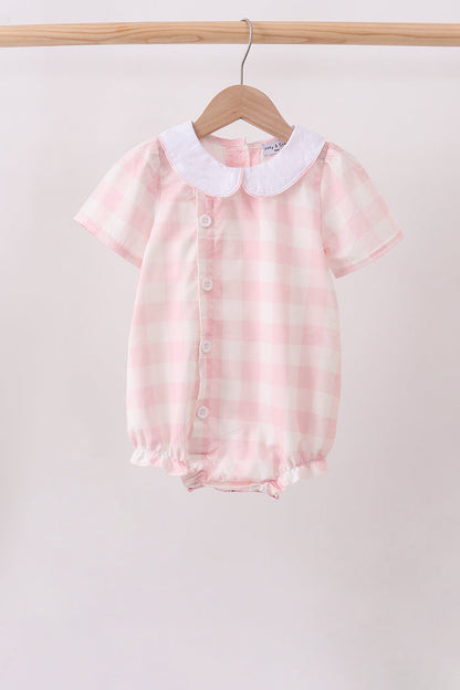 A baby short-sleeve romper in a pink and white gingham check pattern, featuring a white Peter Pan collar and front snap buttons, hanging on a wooden hanger from a clothing rack.