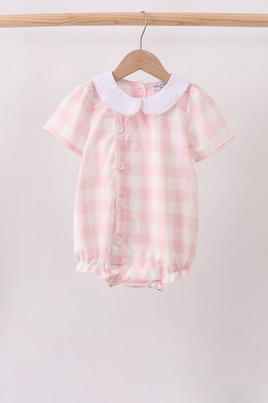 A baby short-sleeve romper in a pink and white gingham check pattern, featuring a white Peter Pan collar and front snap buttons, hanging on a wooden hanger from a clothing rack.