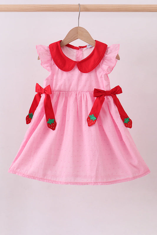 Pink dress with red collar and bow details on a hanger against a light background