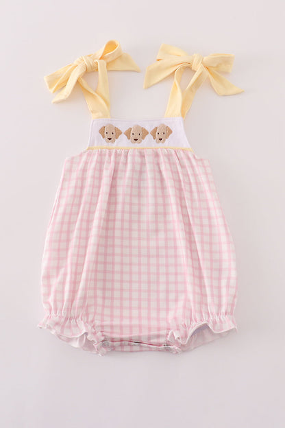 Pink gingham baby romper with yellow straps and bow accents on a light gray background
