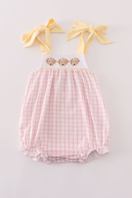 Pink gingham baby romper with yellow straps and bow accents on a light gray background