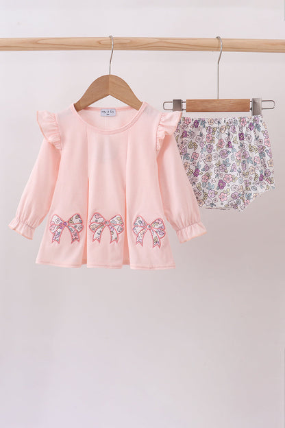 Pink top with bow details and floral shorts on a hanger against a white background