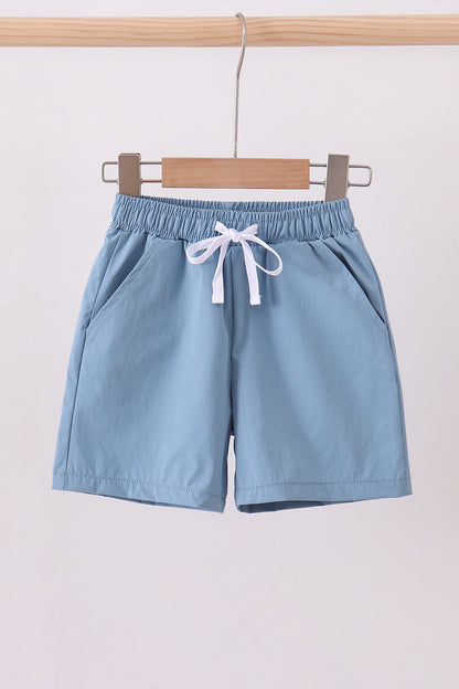 Light blue shorts with a drawstring on a wooden hanger against a white background