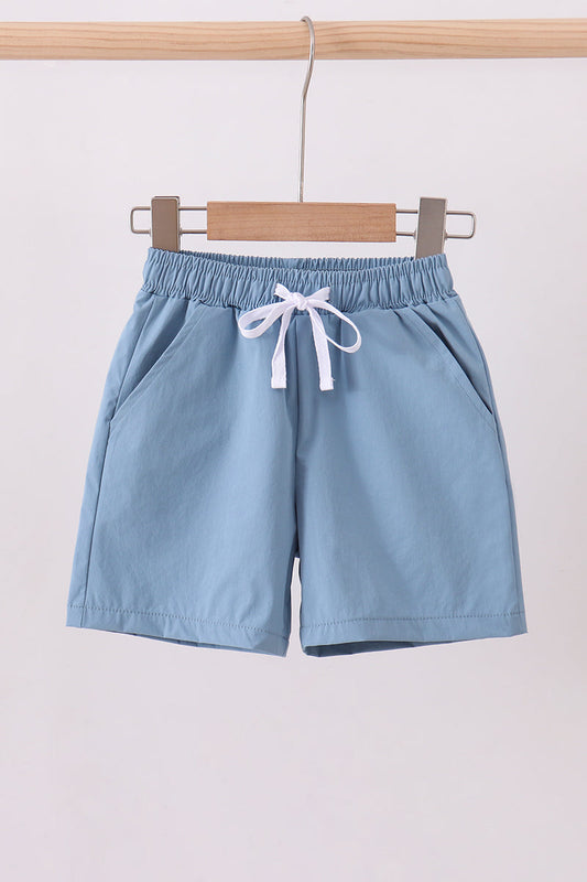 Light blue shorts with a drawstring on a wooden hanger against a white background