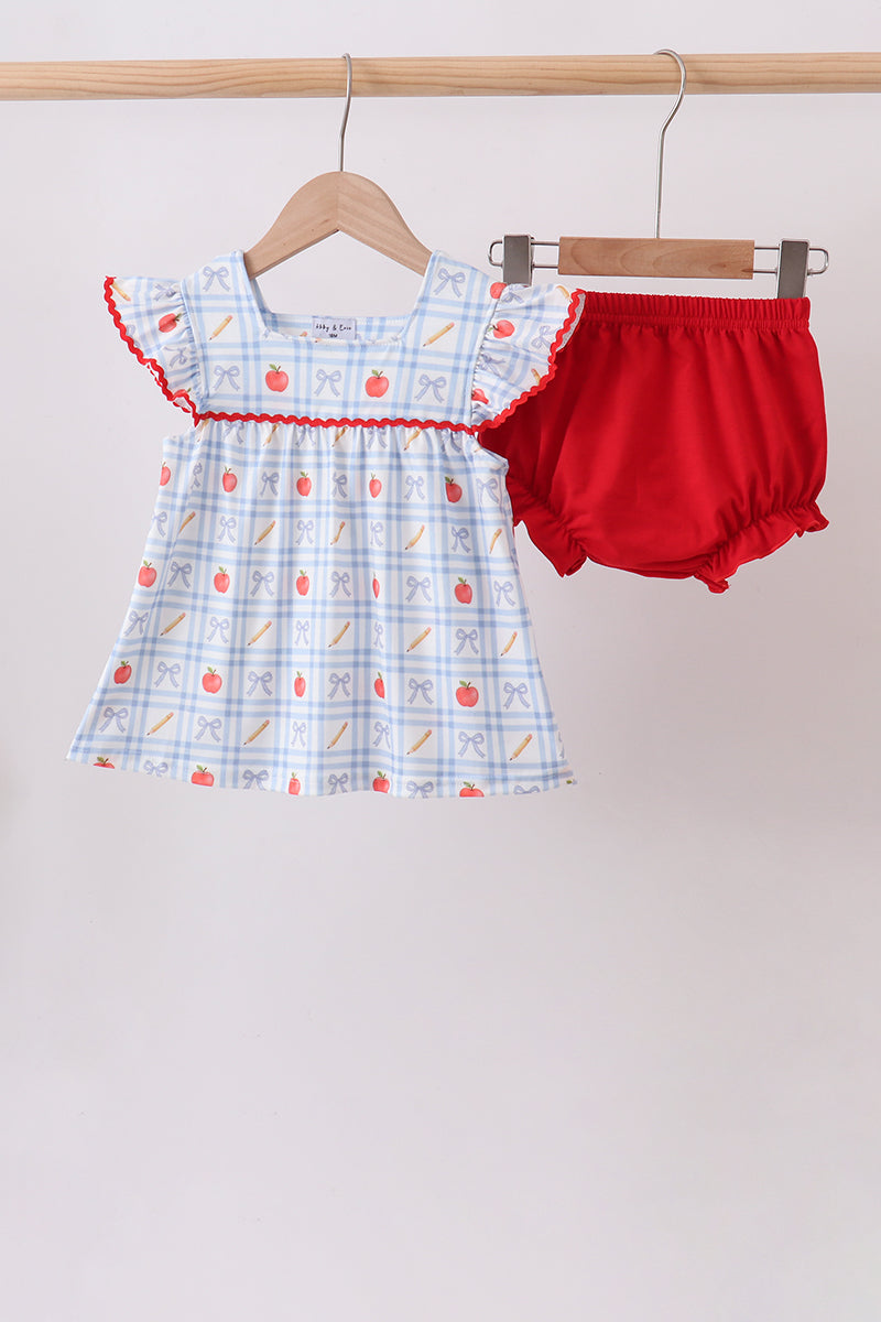 A toddler girl's two-piece outfit hanging on wooden hangers against a plain light background. The set includes a light blue and white gingham patterned top with red ruffle trim and small red/orange fruit motifs, paired with bright red bloomers.