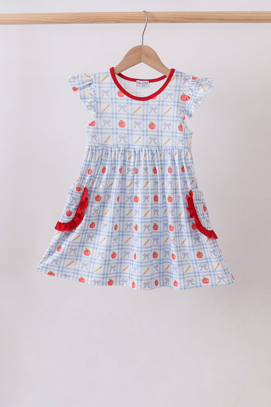 A toddler girl's short-sleeve dress with a white and light blue gingham pattern, decorated with red apple motifs and red ruffle trim, hanging on a wooden hanger against a plain light gray wall.