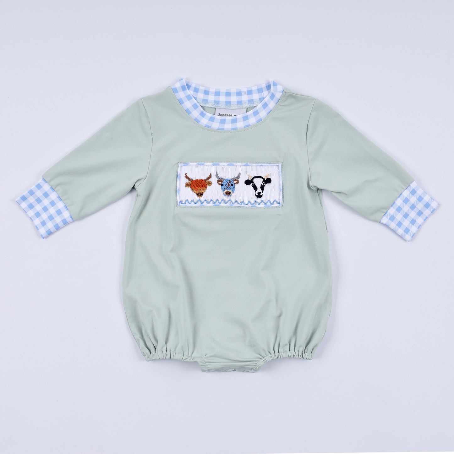Light green baby romper with checkered sleeves and cow design on a light gray background