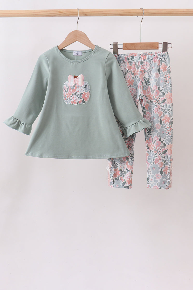 A children's two-piece clothing set hanging on wooden hangers against a plain light background. The set includes a sage green long-sleeve top with a floral bunny patch on the chest and matching floral print pants.