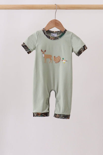 A baby short-sleeve romper in sage green, hanging on a wooden hanger. The romper features a woodland-themed graphic of a deer, turkey, and duck on the chest, with camouflage-patterned trim on the collar, cuffs, and hems.