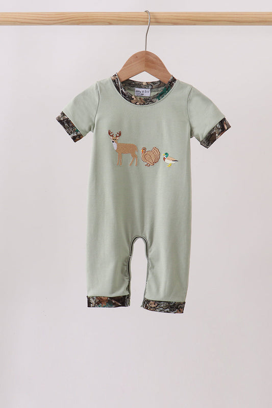 A baby short-sleeve romper in sage green, hanging on a wooden hanger. The romper features a woodland-themed graphic of a deer, turkey, and duck on the chest, with camouflage-patterned trim on the collar, cuffs, and hems.