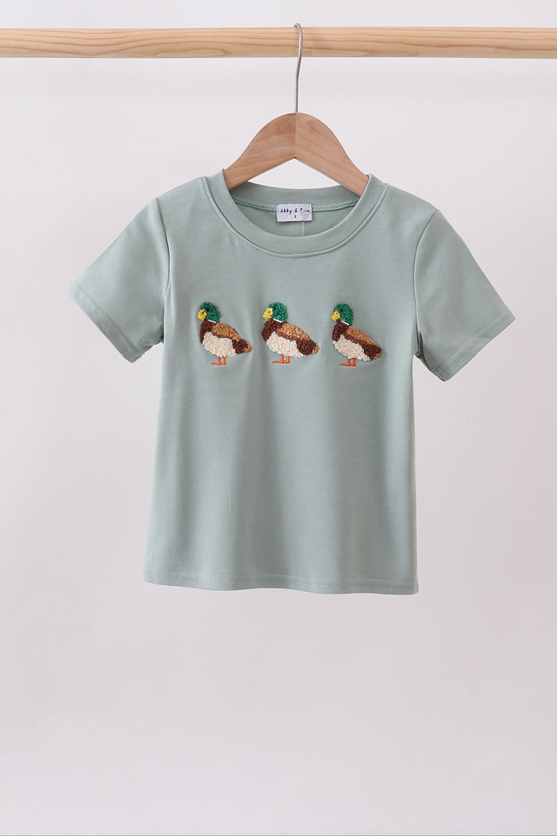 A light sage green short-sleeve t-shirt hanging on a wooden hanger, featuring three embroidered mallards across the chest.