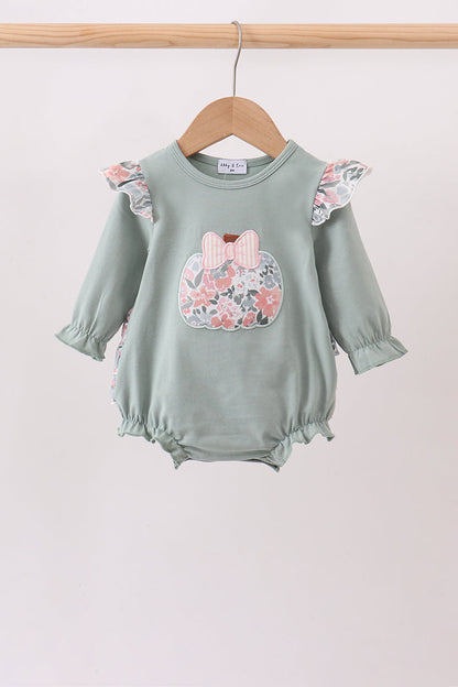 A baby long-sleeve romper in sage green, hanging on a wooden hanger. The romper features ruffled sleeves and hem, a floral applique chest design with a pink bow, and ruffled trim along the side seams.