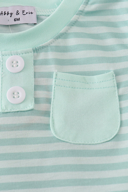 Close-up of a baby outfit with green and white stripes, buttons, and a pocket.