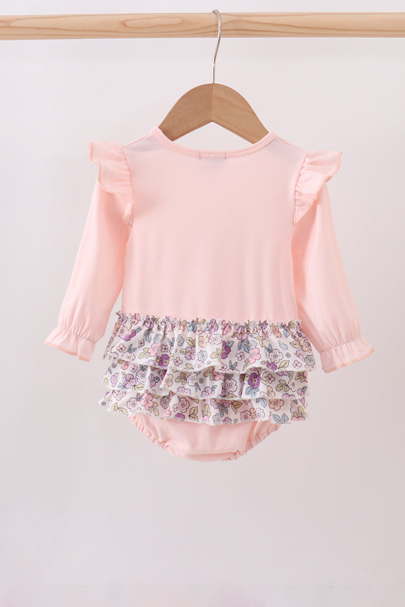Pink top and floral bloomers on a wooden hanger against a light gray background