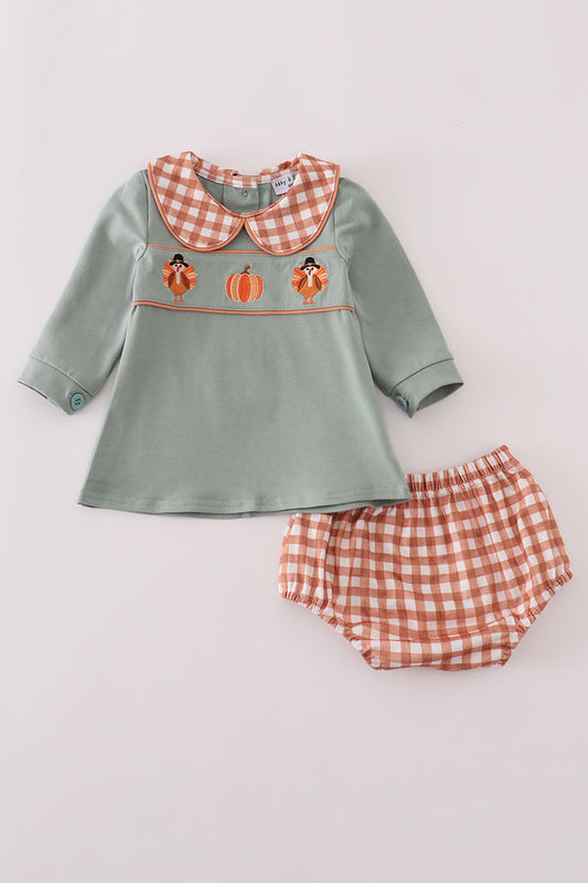 Children's outfit with green top and red checkered shorts on a light gray background